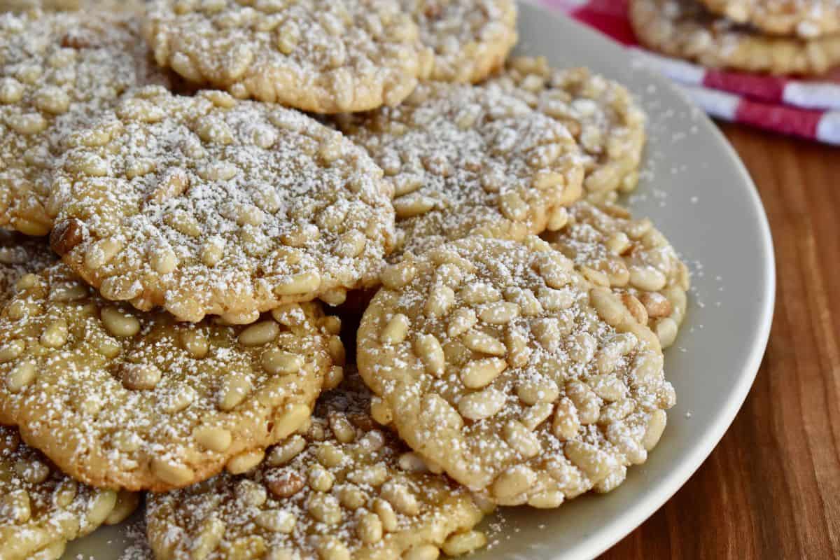 Pignoli cookies made with almond paste and pine nuts on a plate topped with powdered sugar. 
