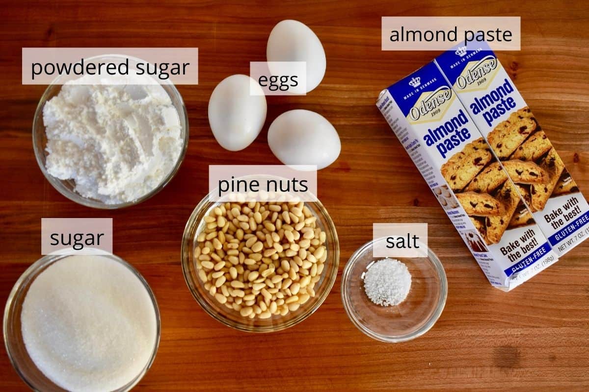 ingredients needed to make the recipe including almond paste, eggs, sugar, salt, and pine nuts. 