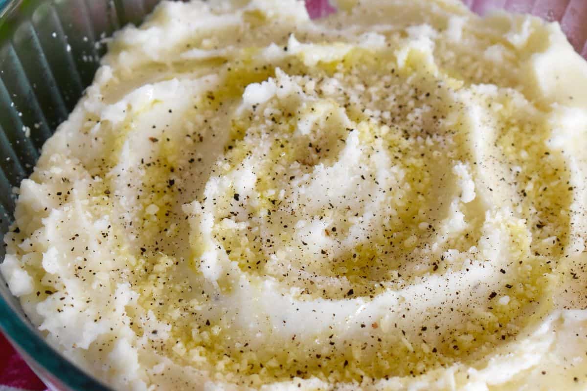 Cacio e Pepe mashed potatoes in a glass bowl with parmesan and black pepper sprinkled on top. 