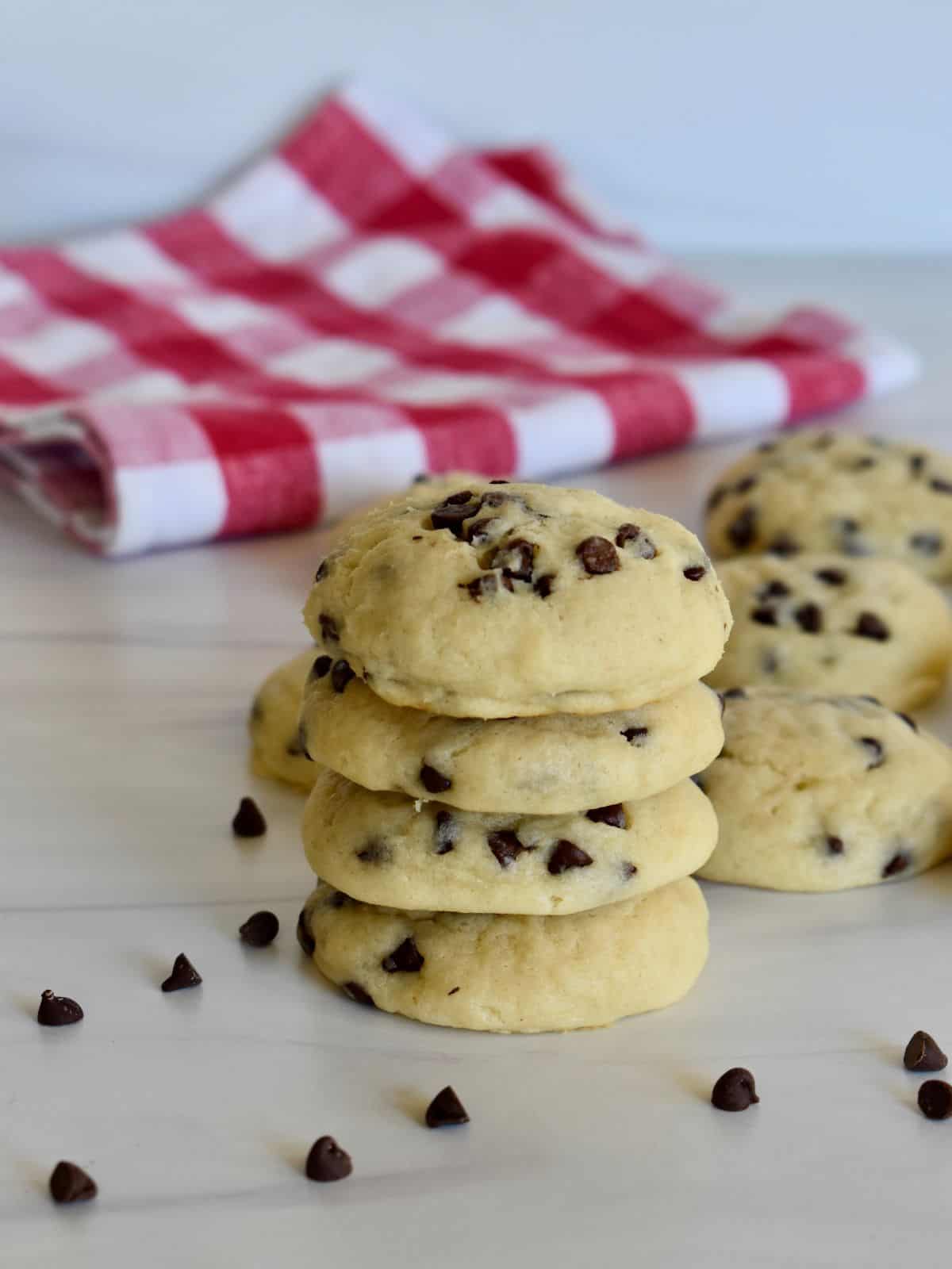 stack of chocolate chip ricotta cookies on a counter with chocolate chips and a checkered napkin. 