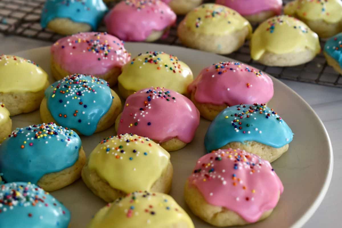 plate of Italian Easter cookies frosted with pink, yellow, and blue frosting and sprinkles. 