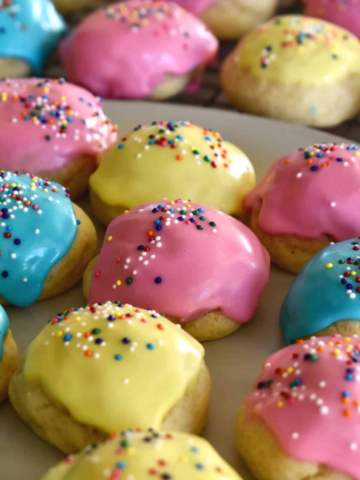 Italian Easter cookies with yellow, pink, and blue frosting on a wire cooling rack. 