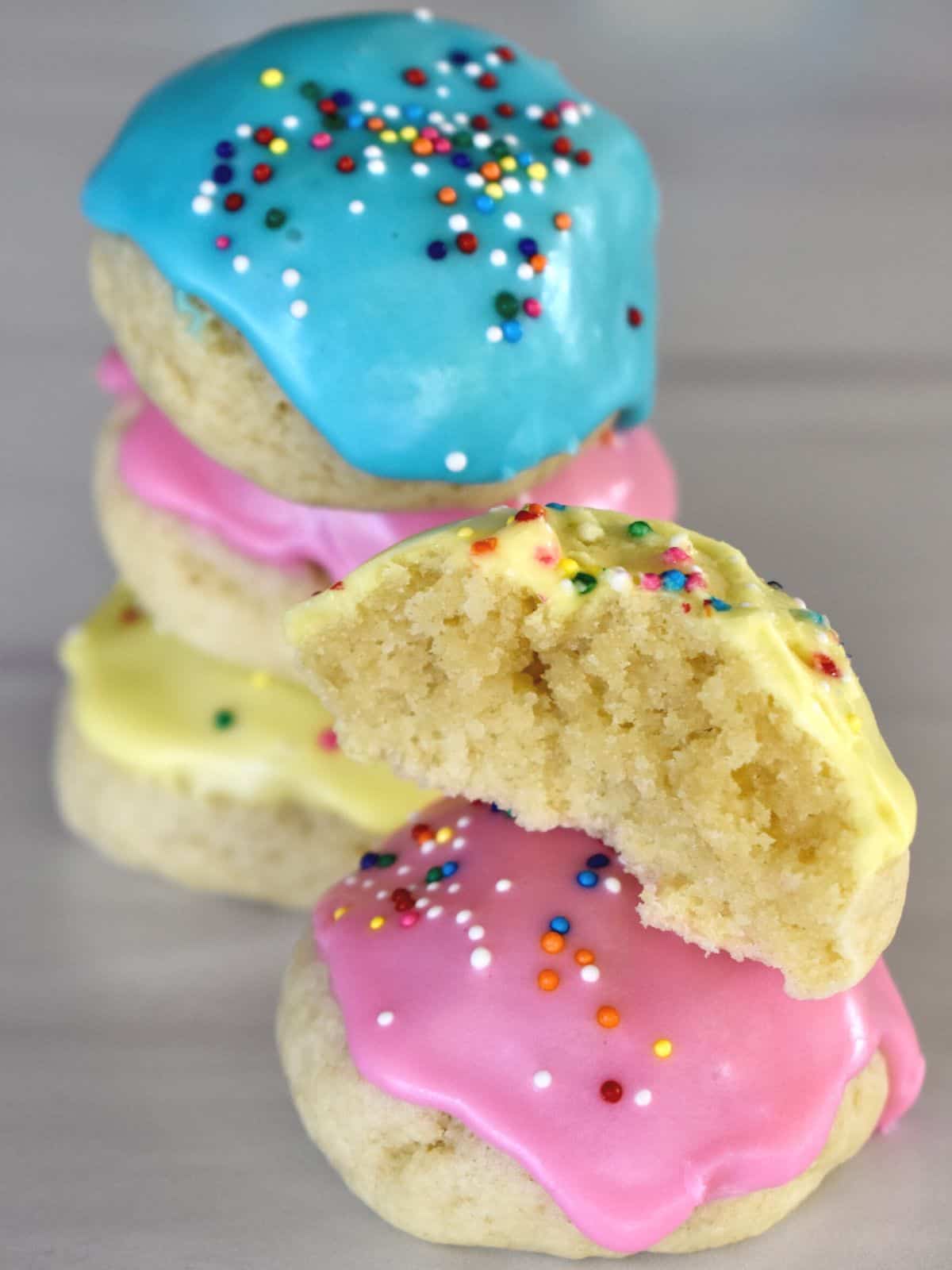 Pink, blue, and yellow frosted Italian Easter Cookies stacked on each other on a countertop.