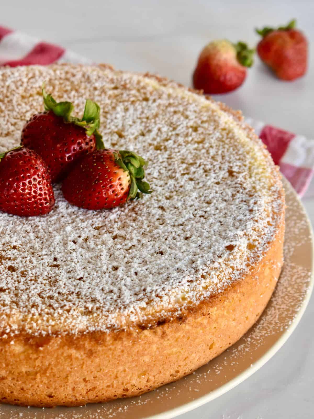 Italian Sponge cake on a plate with powdered sugar and strawberries on top. 