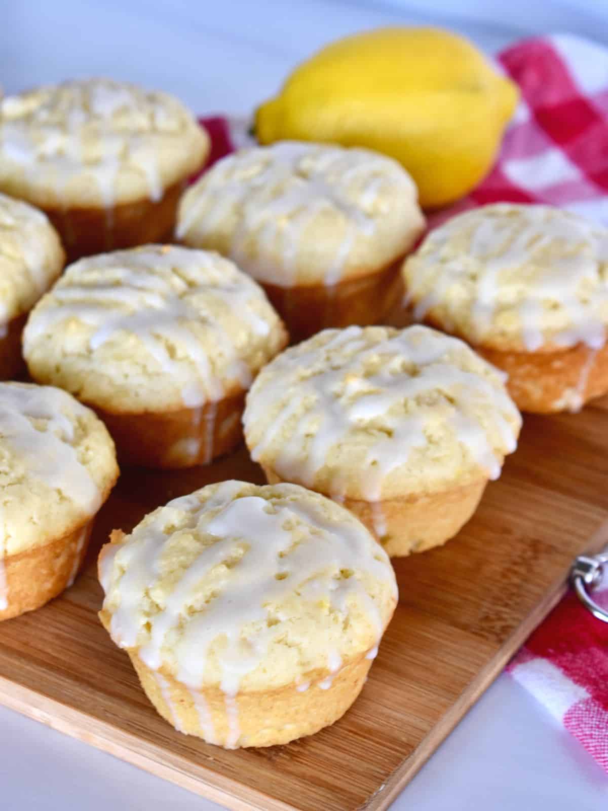 Lemon Ricotta Muffins on a wood cutting board with a checkered napkin and lemon in the background. 