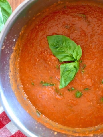 Sugo in a pot with a basil leave on top.