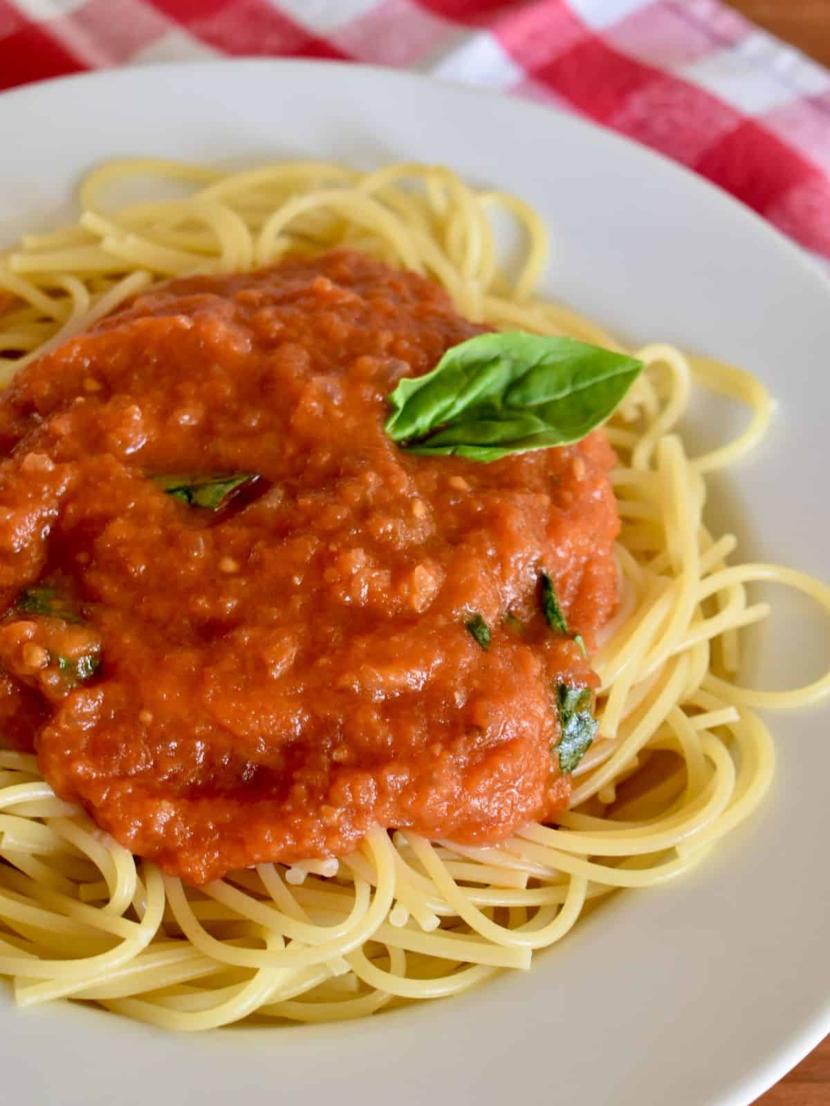 Sugo di pomodoro on spaghetti in a white bowl with a checkered napkin in the background. 