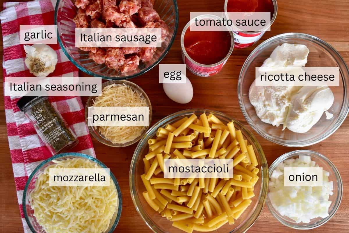 overhead photo of ingredients for recipe including sausage, canned tomato sauce, pasta, ricotta cheese, and onion.