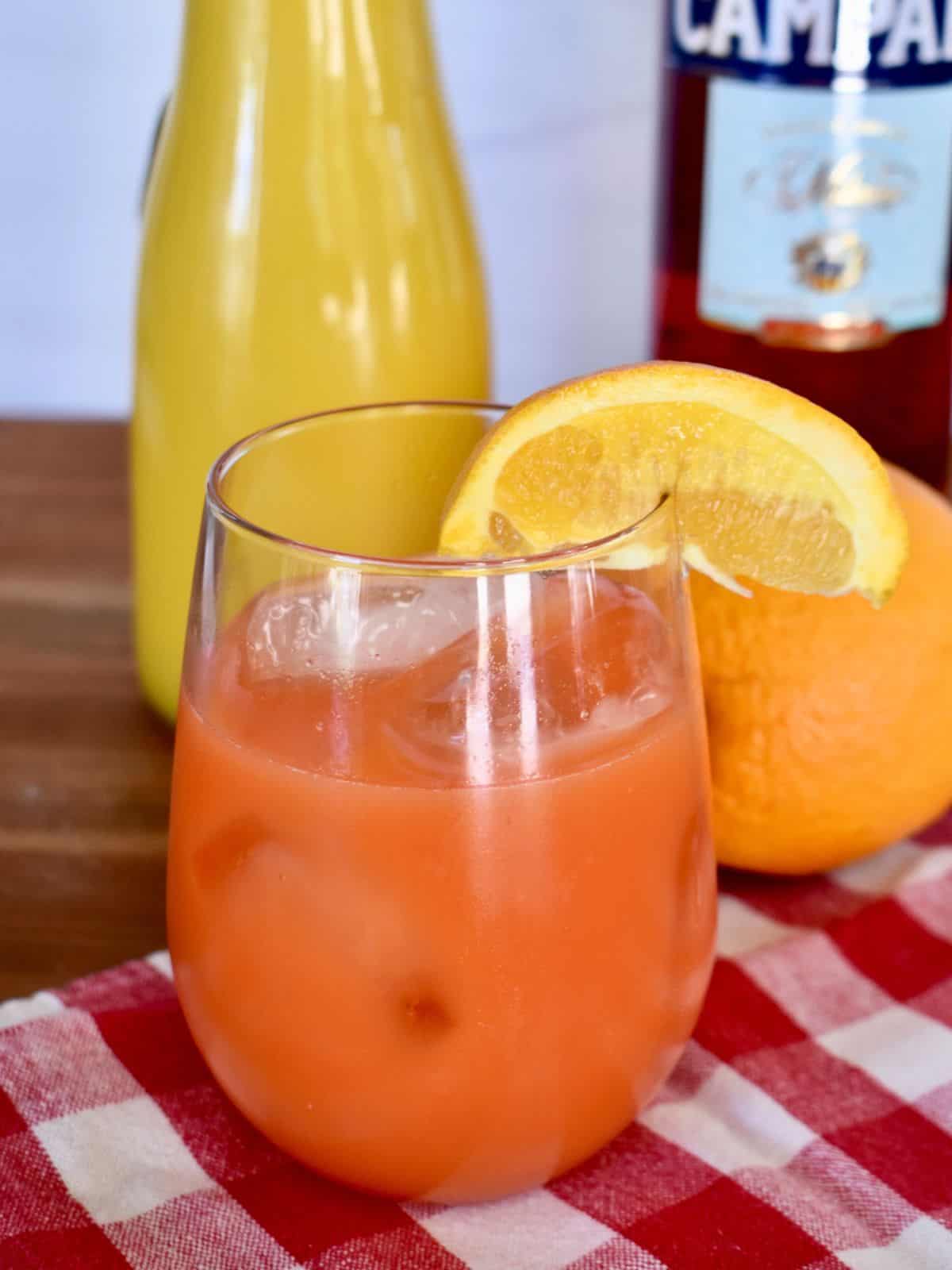 Garibaldi cocktail in a glass with orange juice and Campari in the background. 