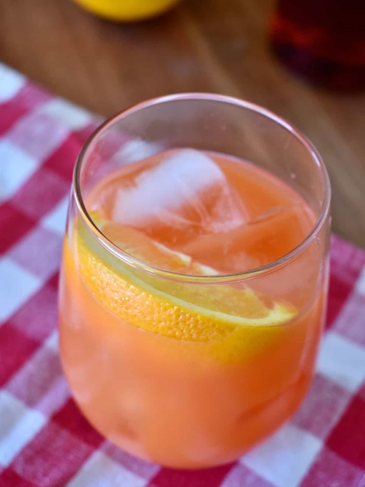 Garibaldi Cocktail in a glass with a wedge of orange on a checkered napkin. 