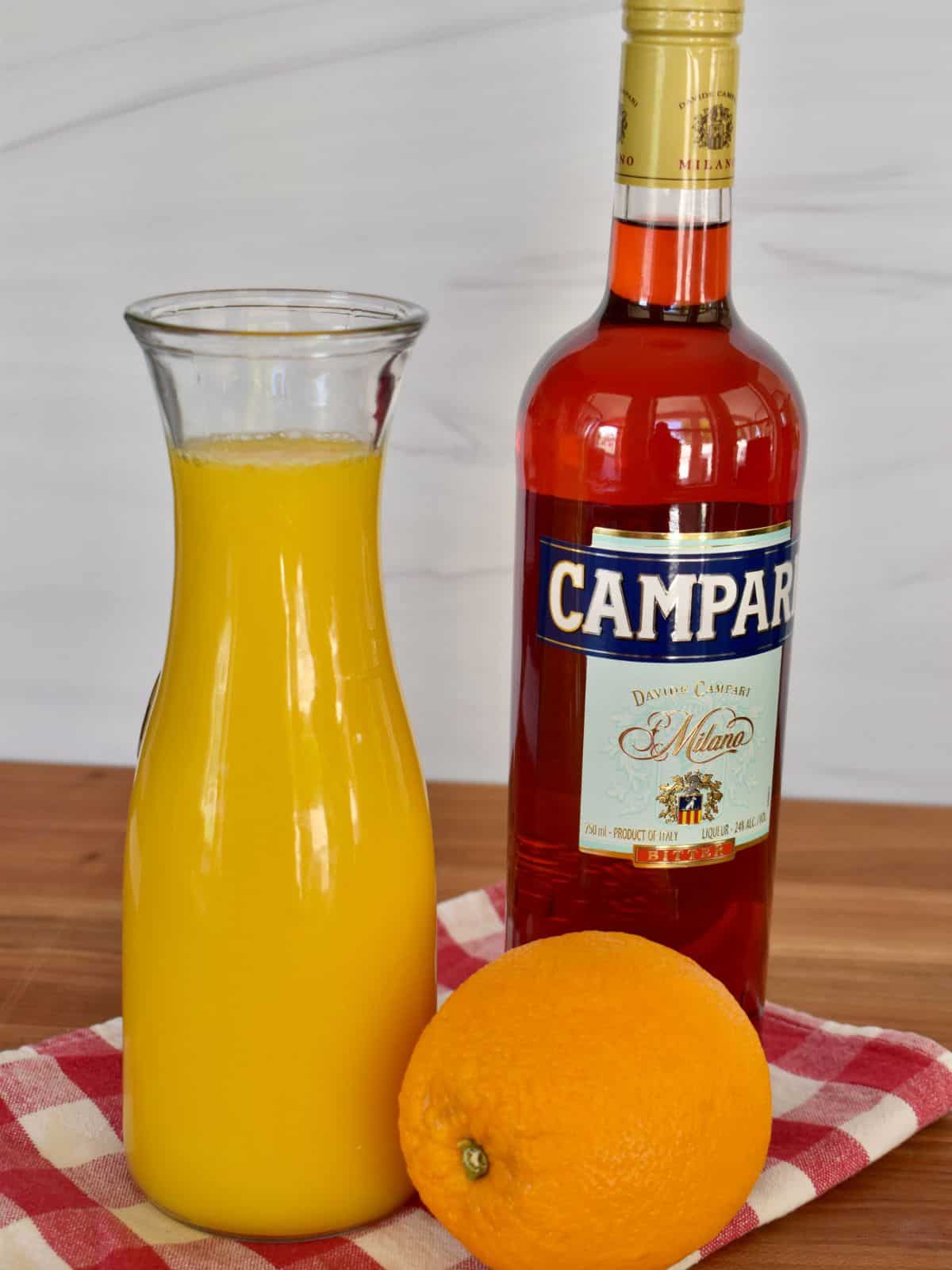 ingredients needed for recipe including fresh orange juice, Campari, and an orange for garnish. 