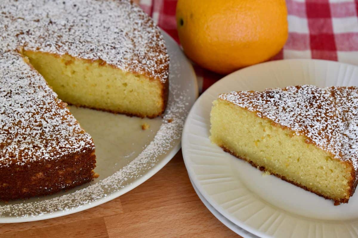 Orange Ricotta Cake on a plate with an orange in the background. 