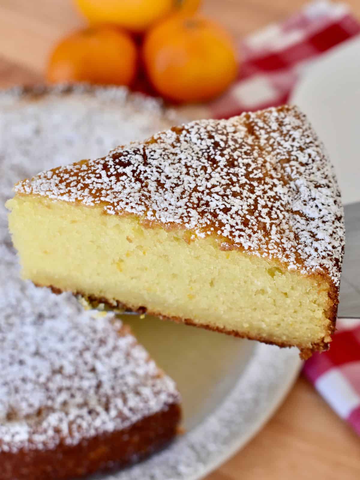 Orange Ricotta Cake slice with oranges in the background. 