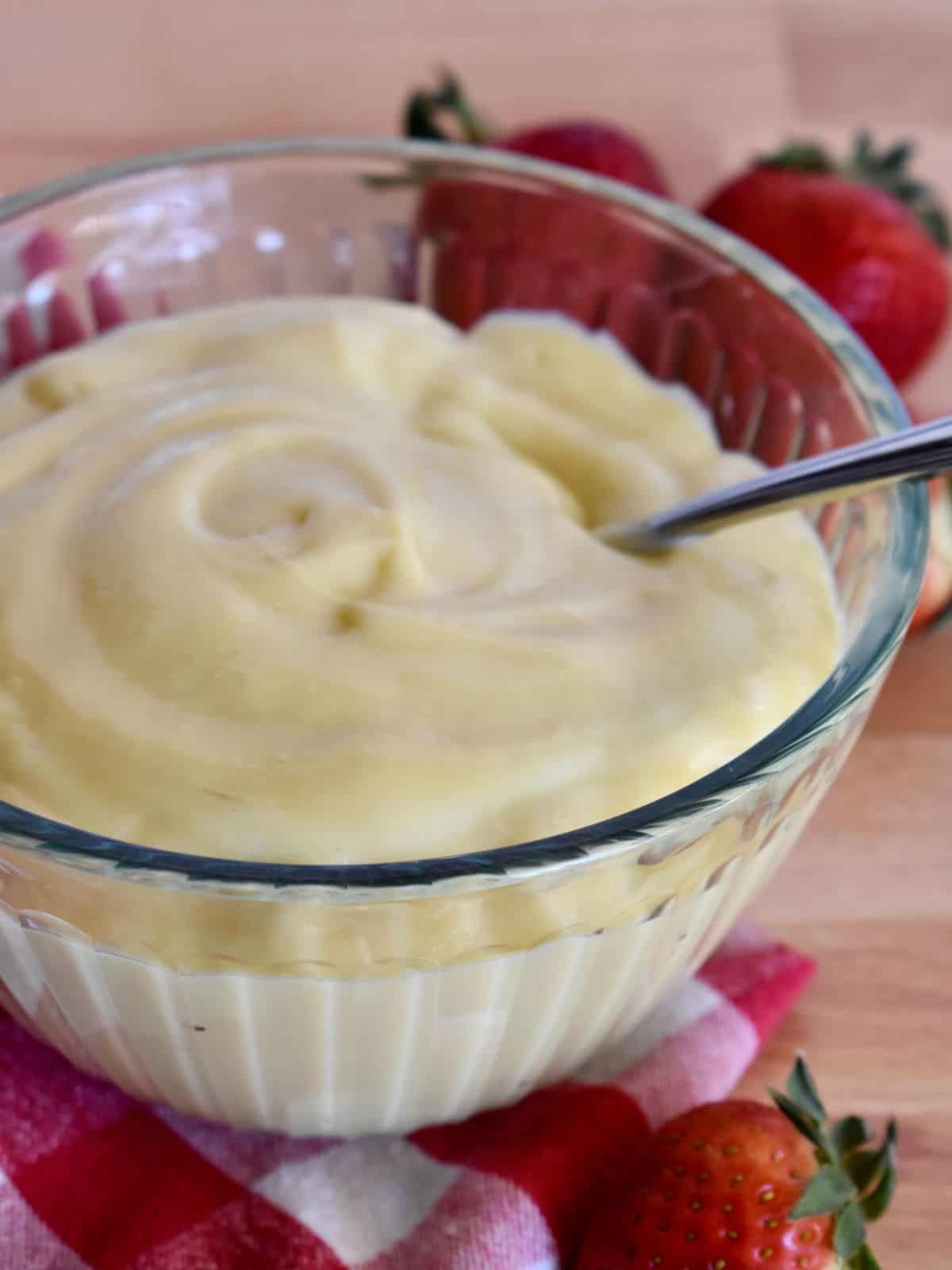 Italian pastry cream in a glass bowl with strawberries in the background. 