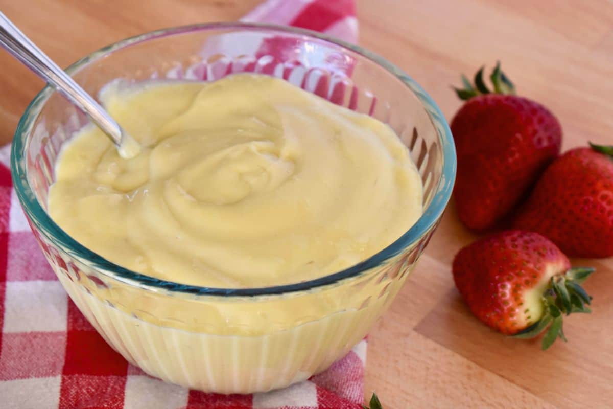 Italian pastry cream in glass bowl with a spoon in it and strawberries in the background. 