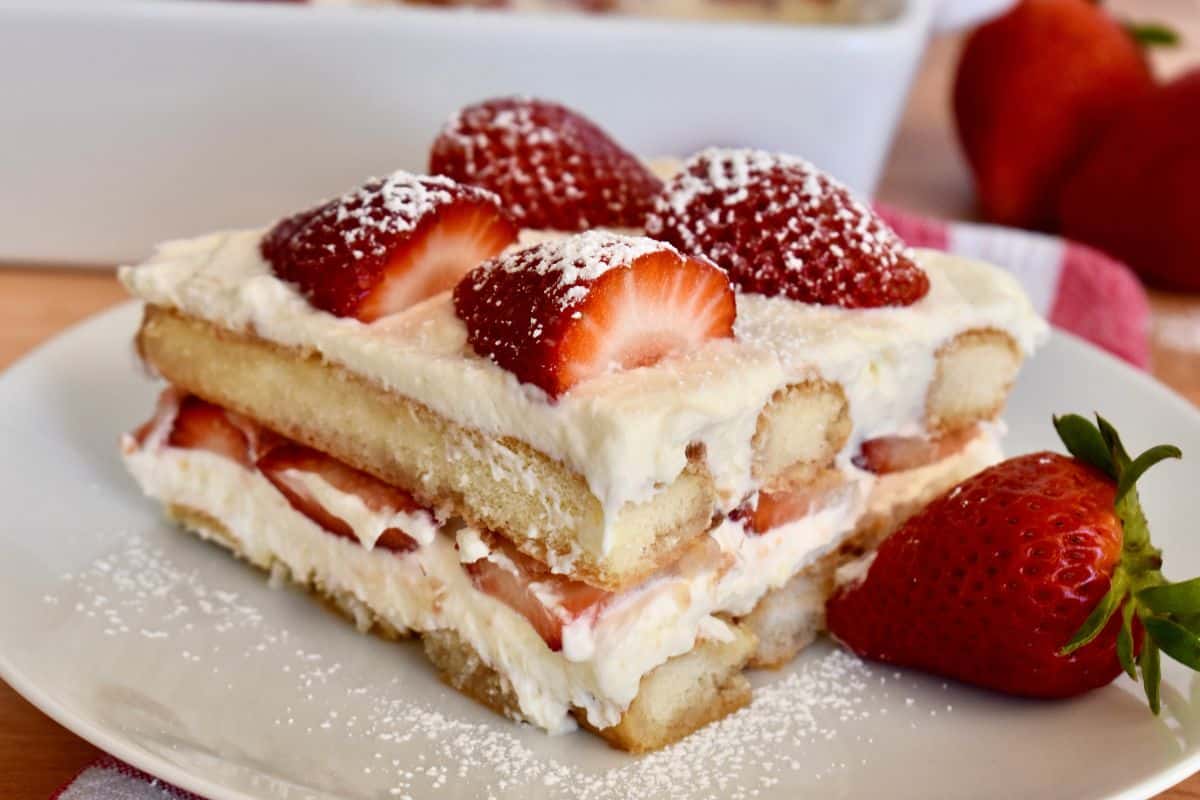 slice of strawberry tiramisu on a white plate with strawberries on top. 
