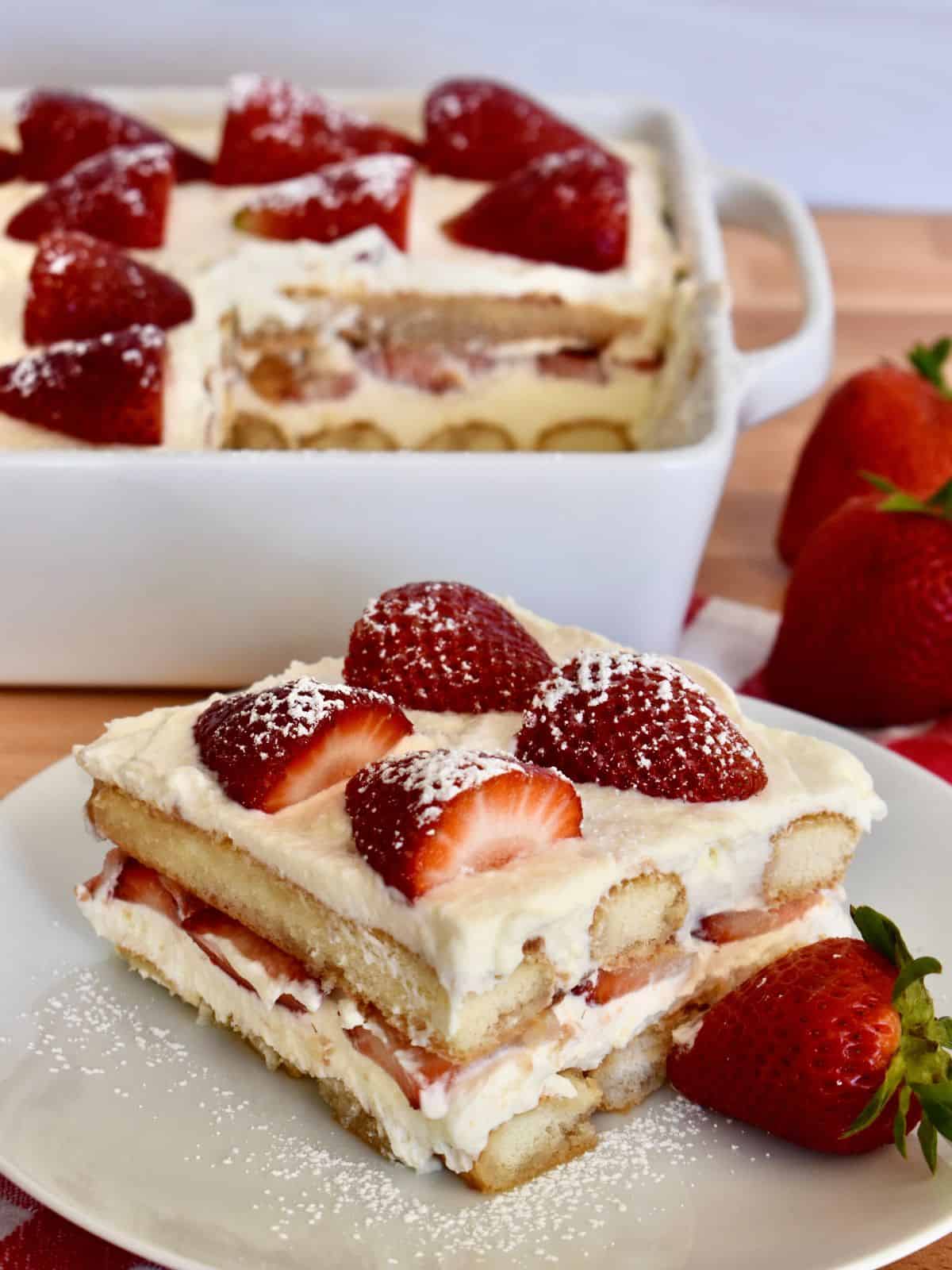 Strawberry Tiramisu on a white plate with a dish of tiramisu in the background. 