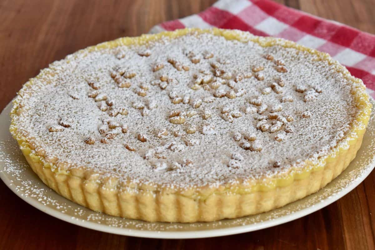 Torta della Nonna with pine nuts and powdered sugar on top on a plate. 