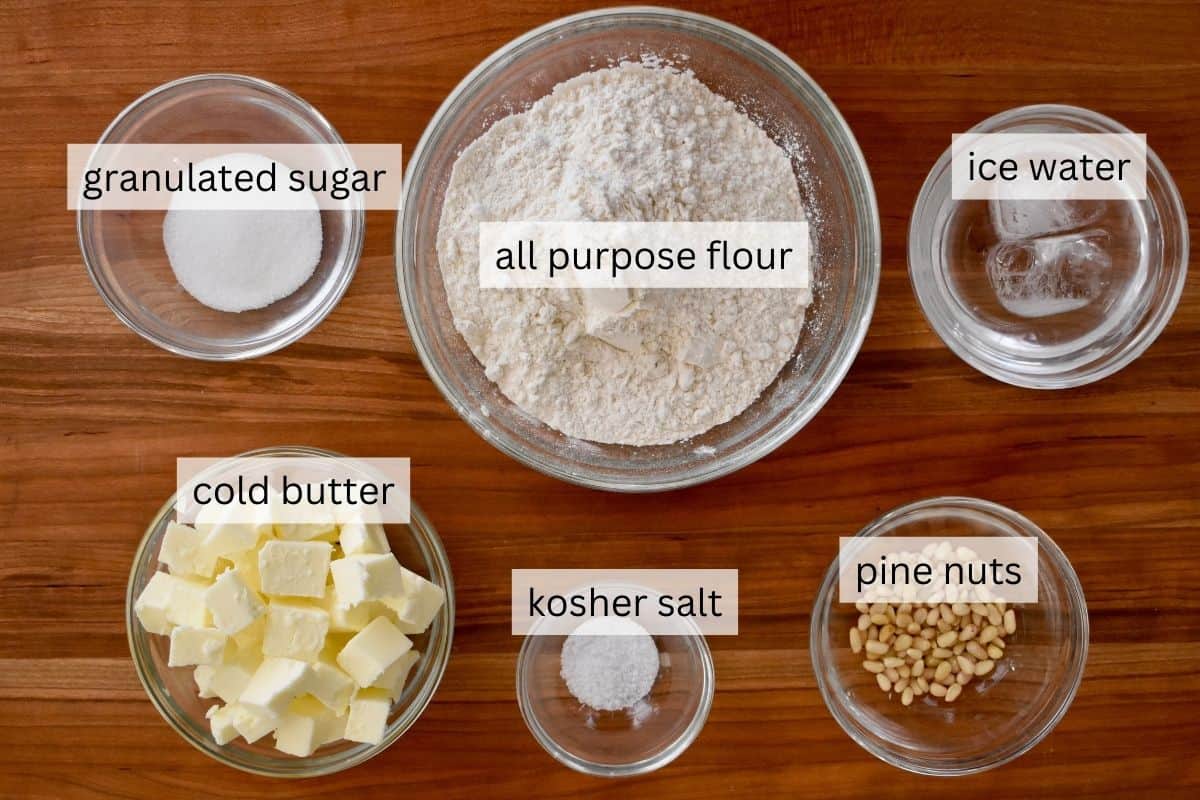 overhead photo of ingredients needed to make pastry crust including butter, flour, sugar, water, salt, and pine nuts. 