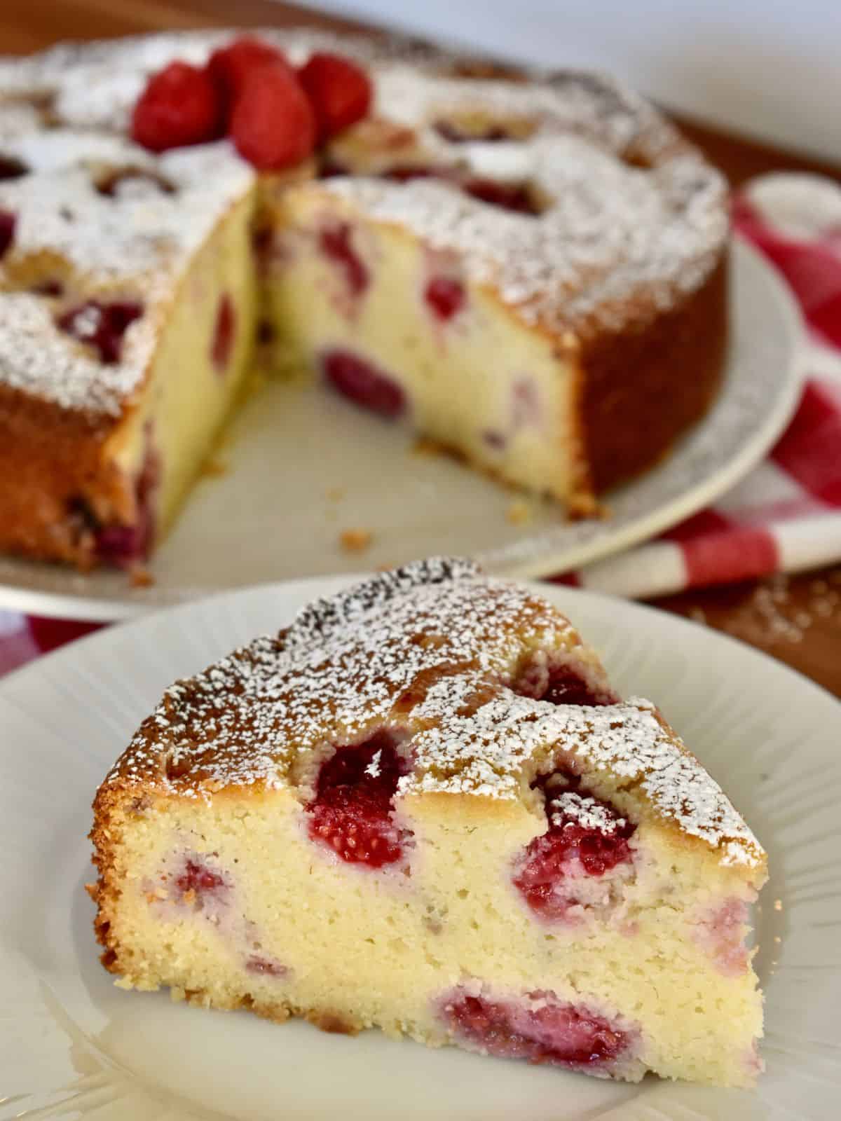 Raspberry Ricotta Cake on a white plate with a checkered napkin in the background. 