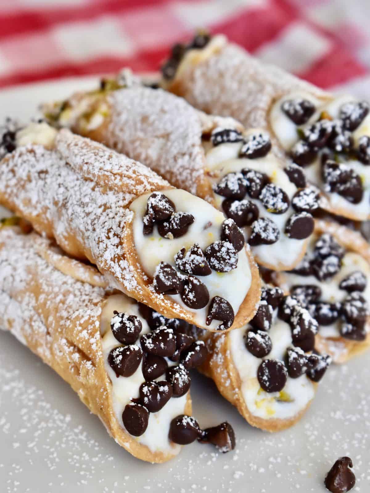 Authentic Italian Ricotta Cannolis on a white plate with powdered sugar on top and a checkered napkin in the background. 