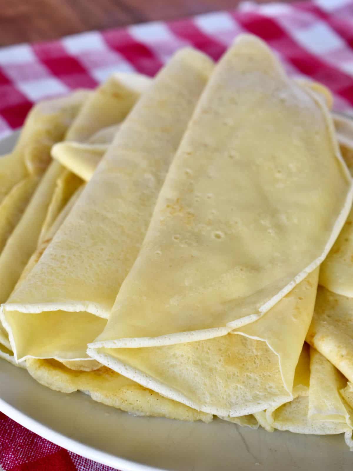 Italian Crepes, Crespelle, on a plate with a checkered napkin underneath. 
