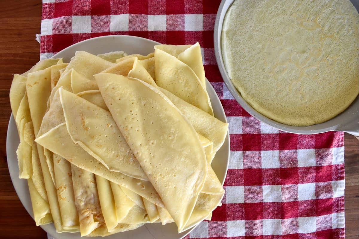 Overhead crespelle on a plate with a crepe pan next to it. 