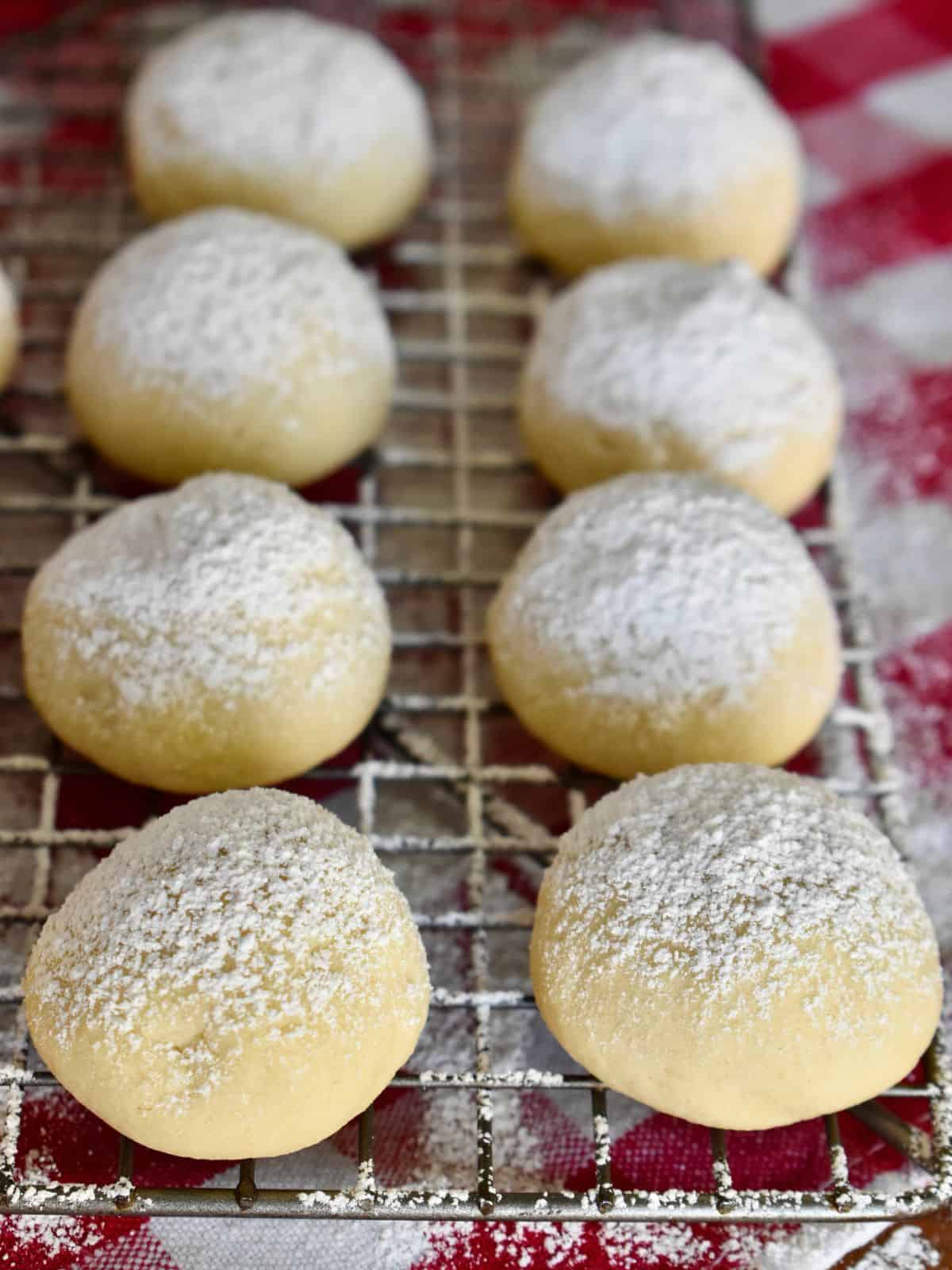 Italian wedding cookies on a wire cooling rack with powdered sugar dusted on top of them.