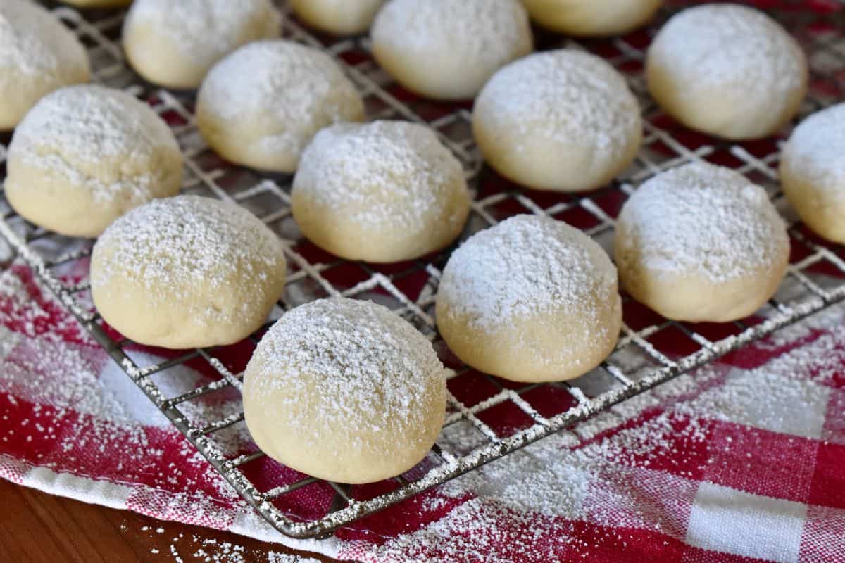Italian wedding cookies on a wire cooling rack with powdered sugar dusted on top of them. 