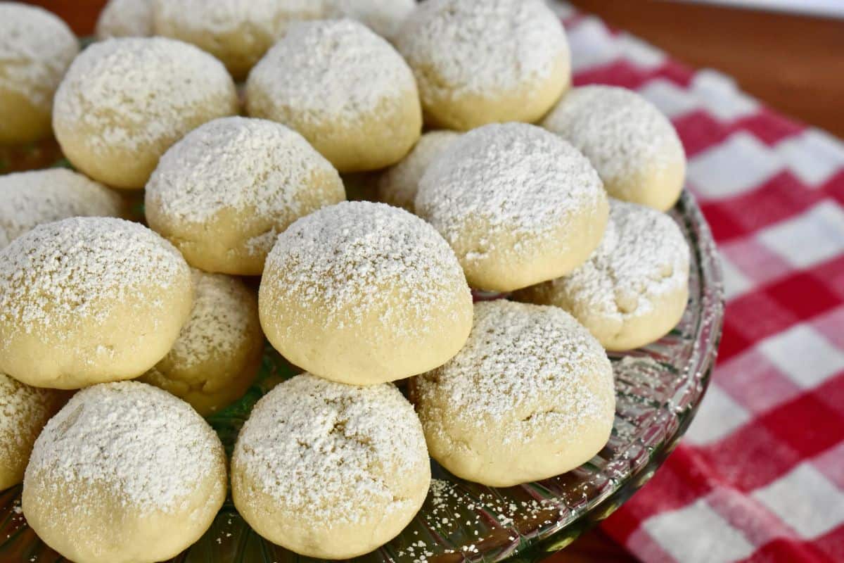 Italian wedding cookies dusted with powdered sugar on a glass cake stand. 
