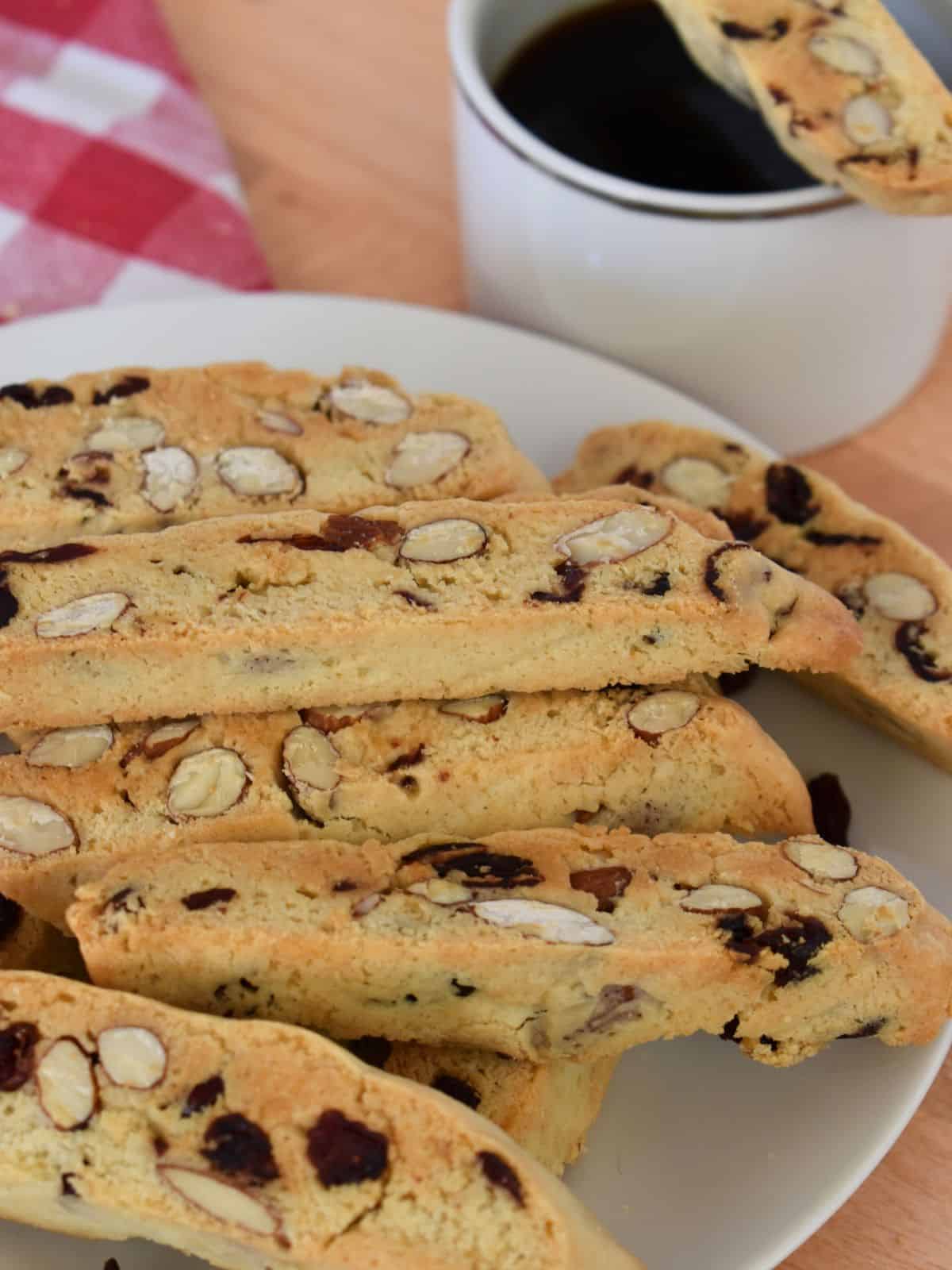 Cranberry Almond Biscotti piled on a plate with a cup of coffee in the background. 