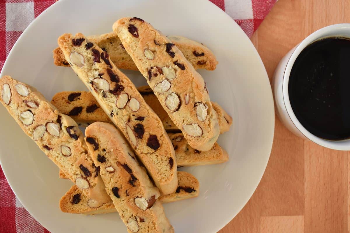 Overhead view of cranberry almond biscotti on a white plate and a cup of coffee next to it. 