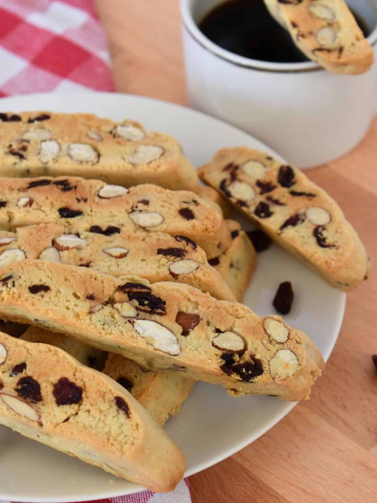 Cranberry Almond Biscotti on a white plate with a cup of coffee next to it. 