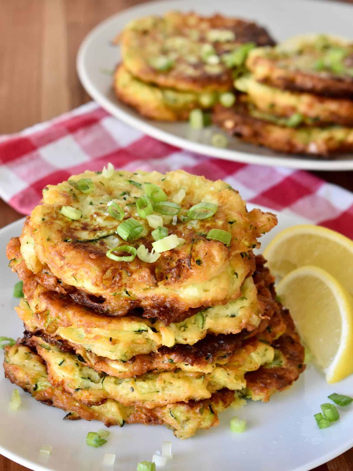 Zucchini Ricotta Fritters stacked on a plate with a wedge of lemon next to it. 