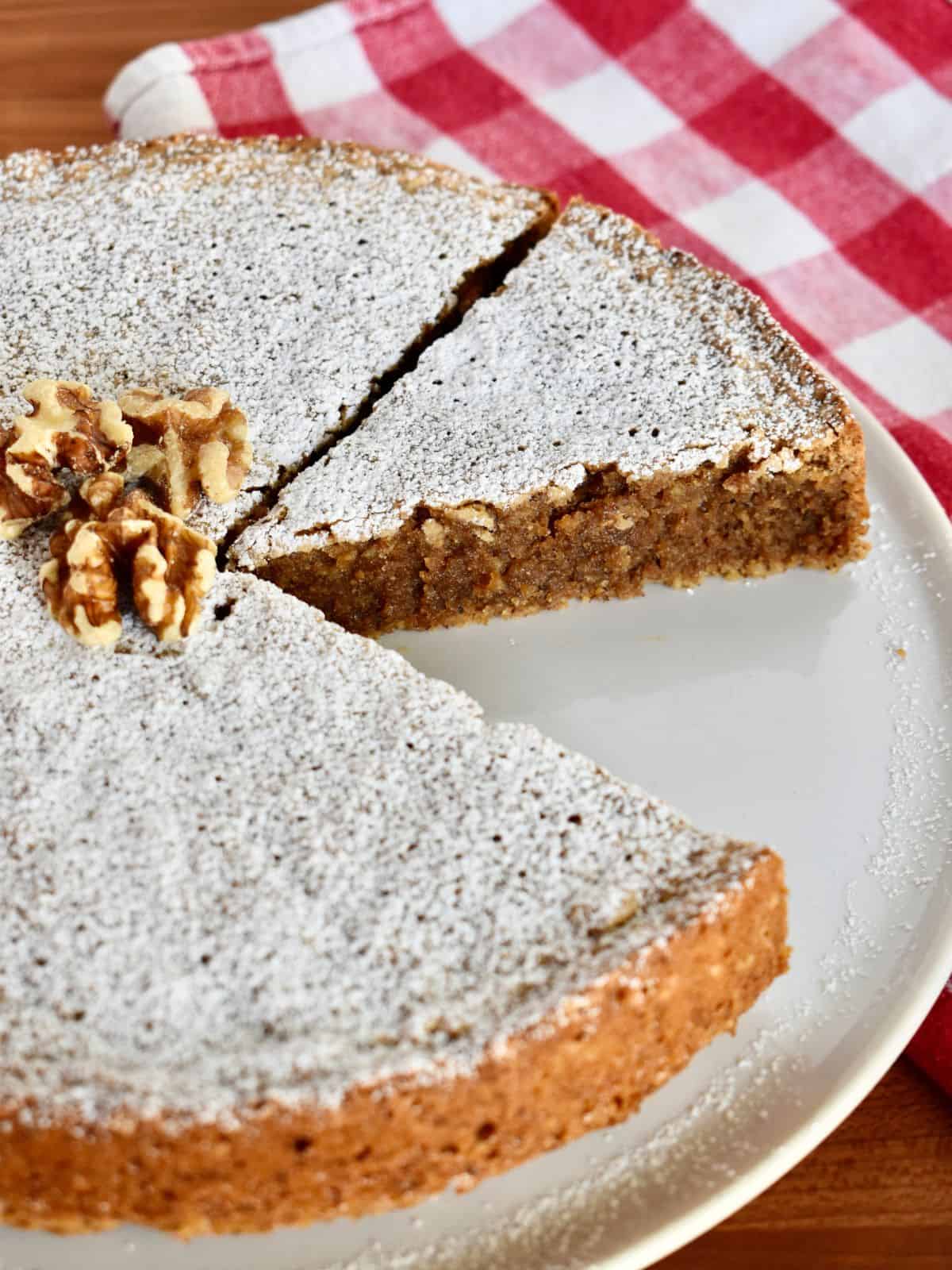 Italian Walnut Cake or Torta di Noci on a white plate with a checkered napkin in the background.