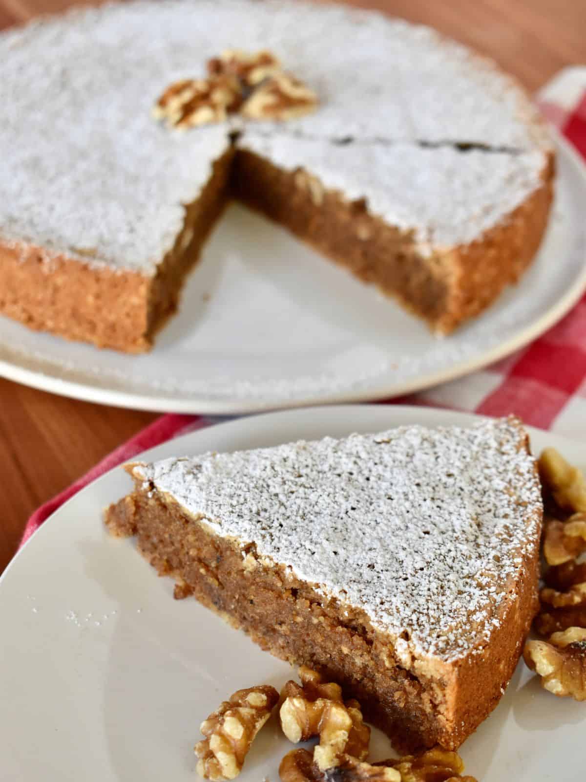Slice of Italian Walnut Cake on a white plate with a cake in the background. 