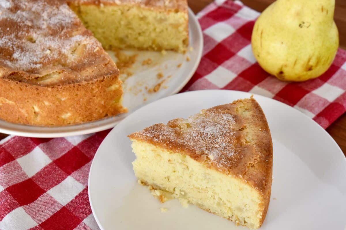 Italian Pear Cake slice on a white plate with a pear in the background. 