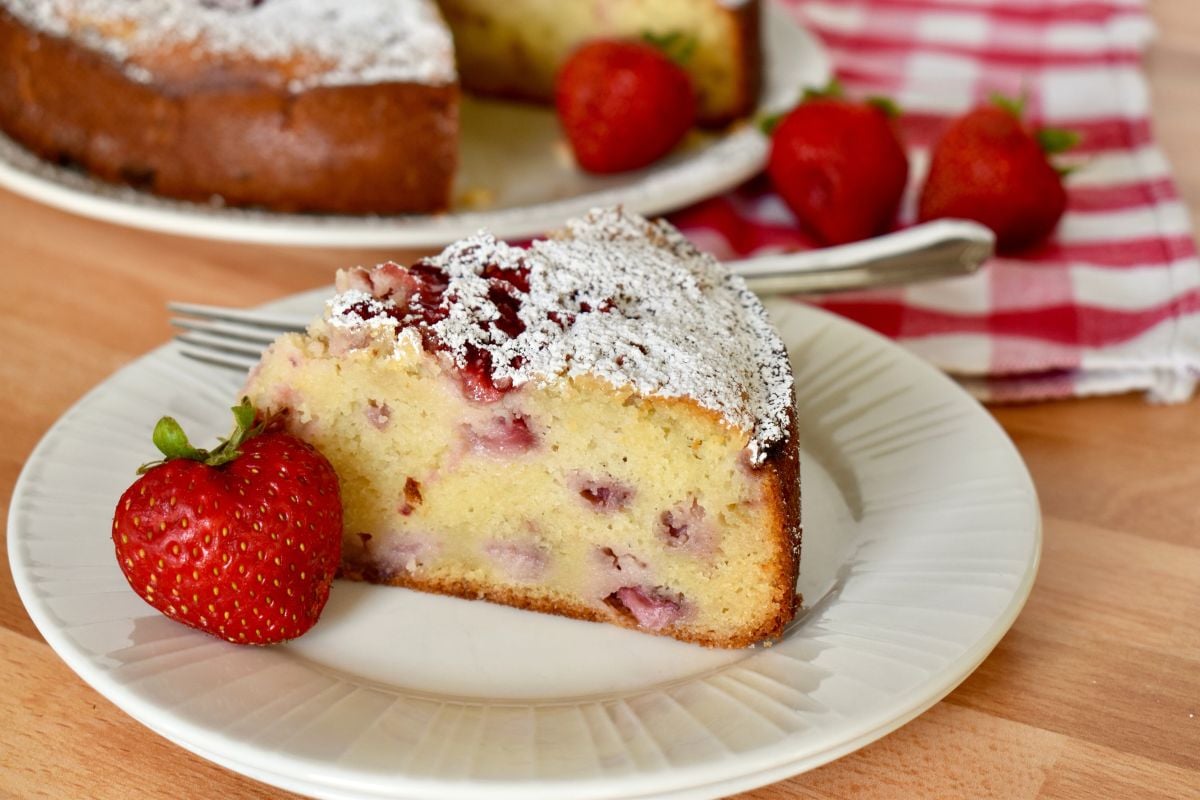 Strawberry Ricotta cake on a white plate with a checkered napkin in the background. 