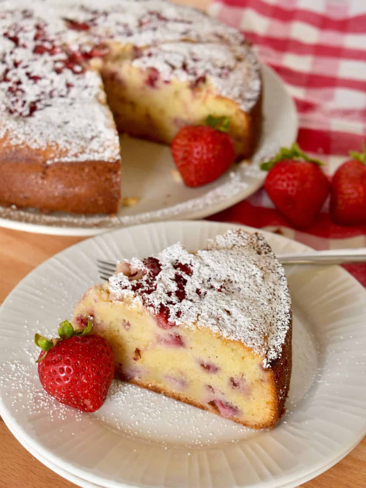Strawberry Ricotta cake on a white plate with a cake in the background. 