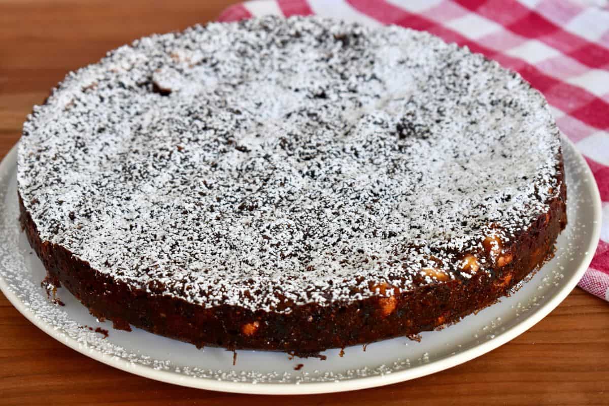 Whole Panforte di Siena on a white plate with powdered sugar sprinkled on top. 