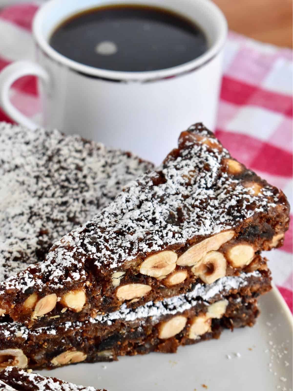 Wedges of sliced panforte stacked on each other with a cup of coffee behind them. 