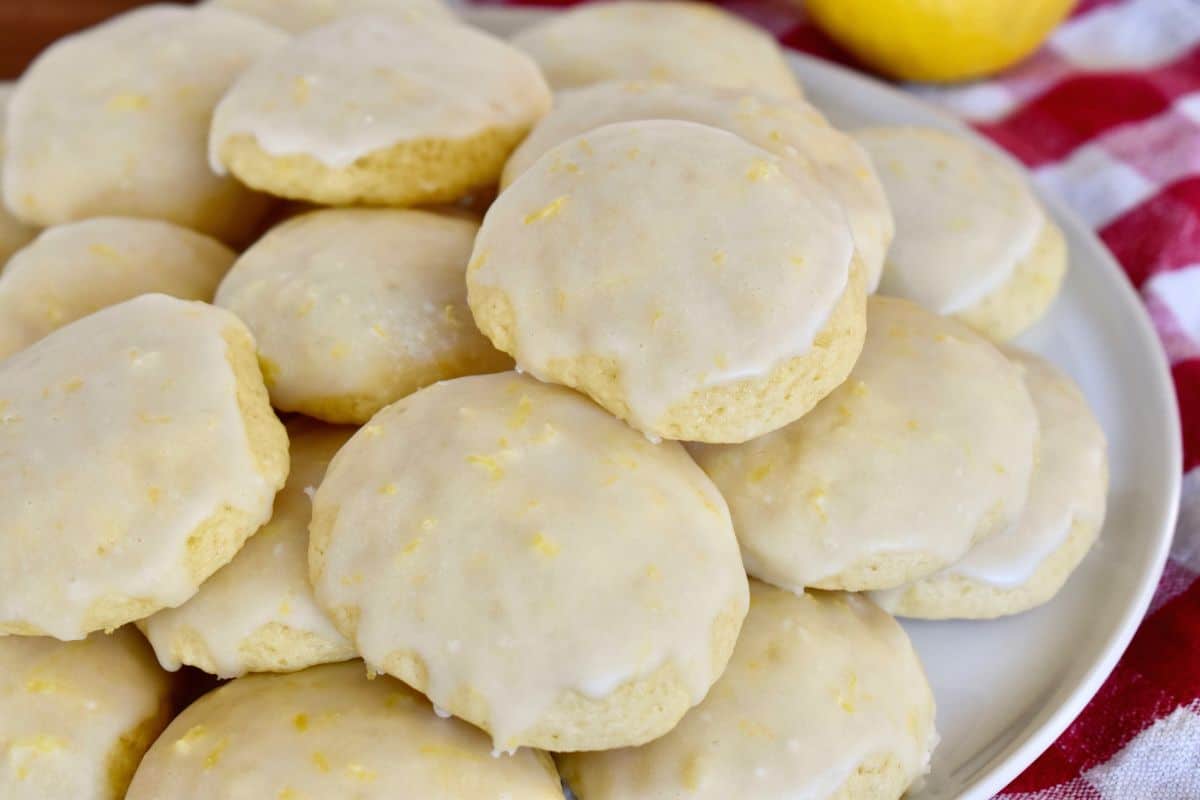 Italian Lemon Drop cookies on a white plate with a checkered napkin and lemons in the background. 