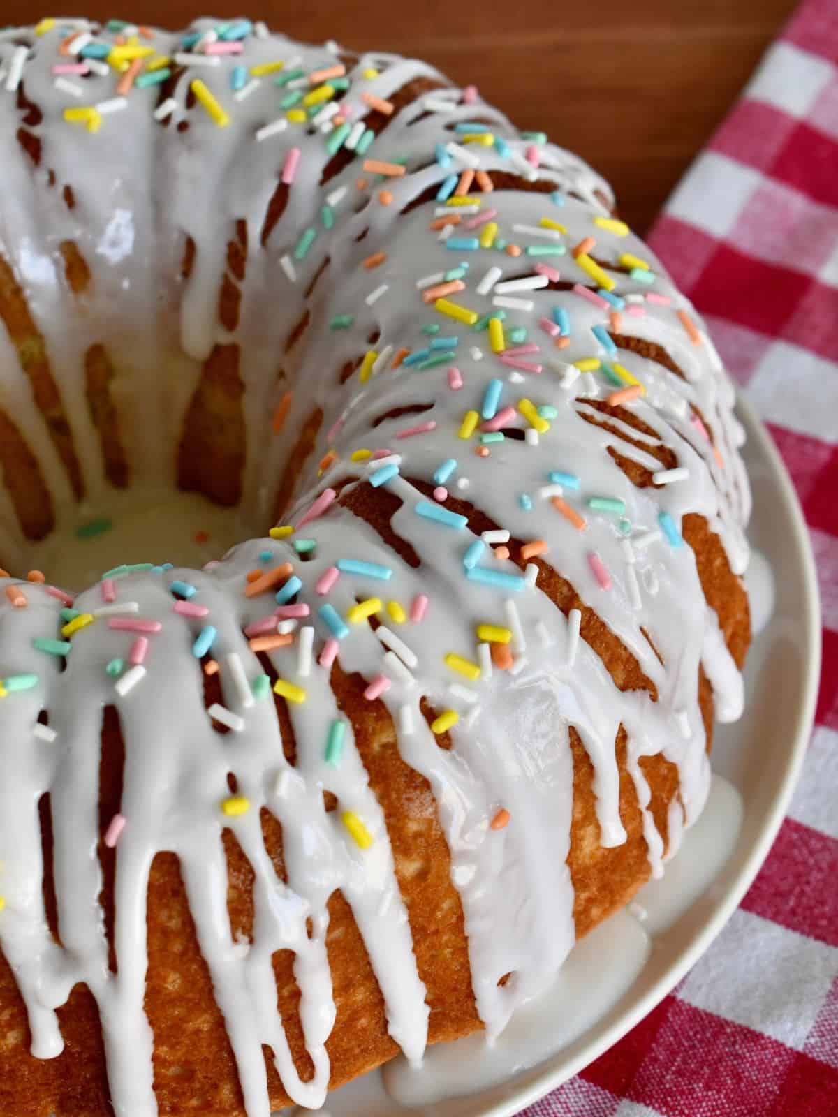 Italian Easter Cake with glaze and pastel sprinkles on a white plate with a checkered napkin underneath.