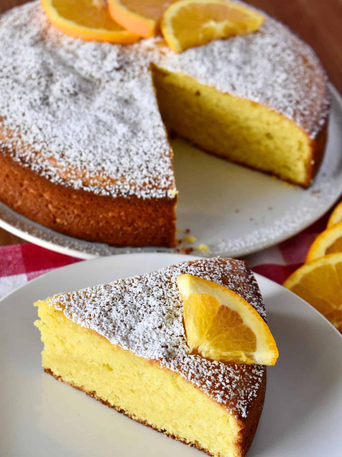 Italian Orange Cake on a white plate with orange slices and powdered sugar on top. 