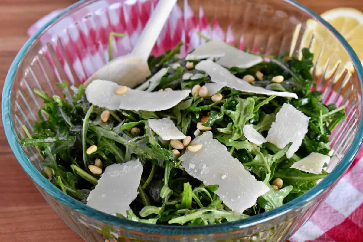 Italian Arugula Salad with lemon, parmesan cheese, and pine nuts in a glass bowl. 
