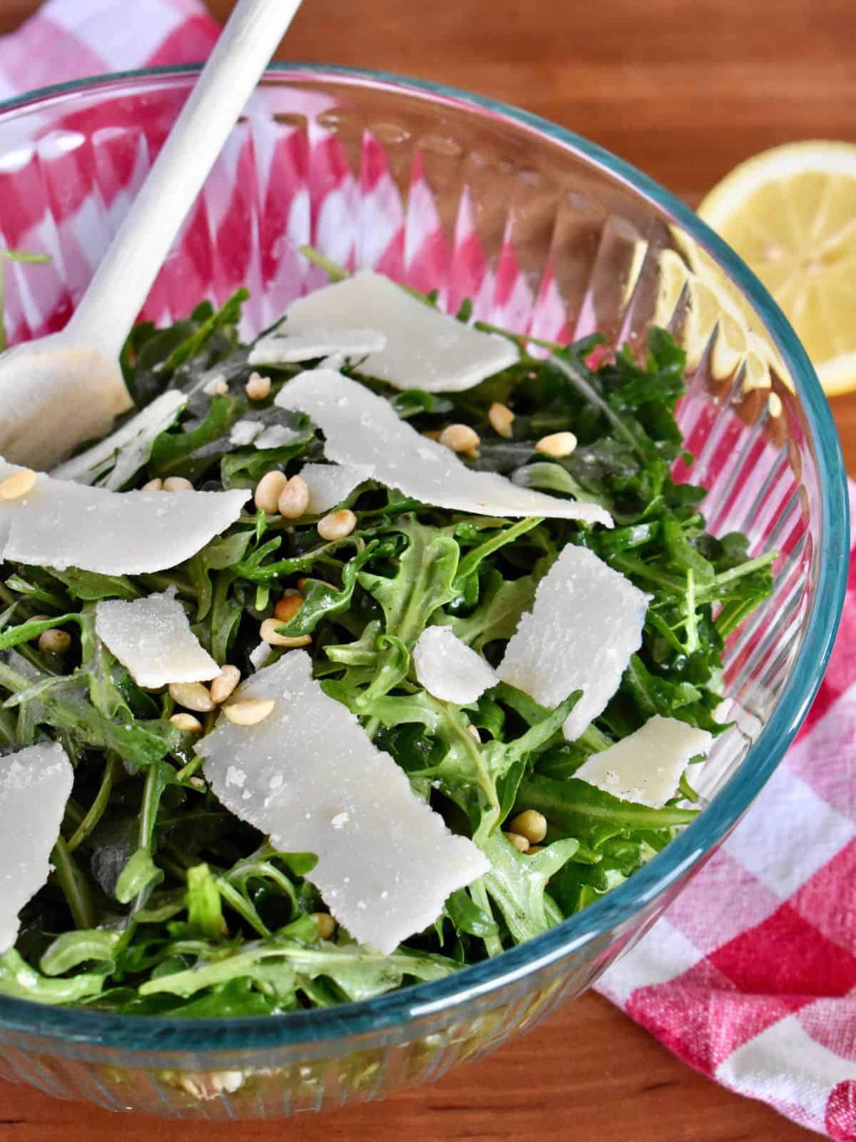 Italian Arugula Salad with pine nuts and shaved parmesan in a large glass bowl. 