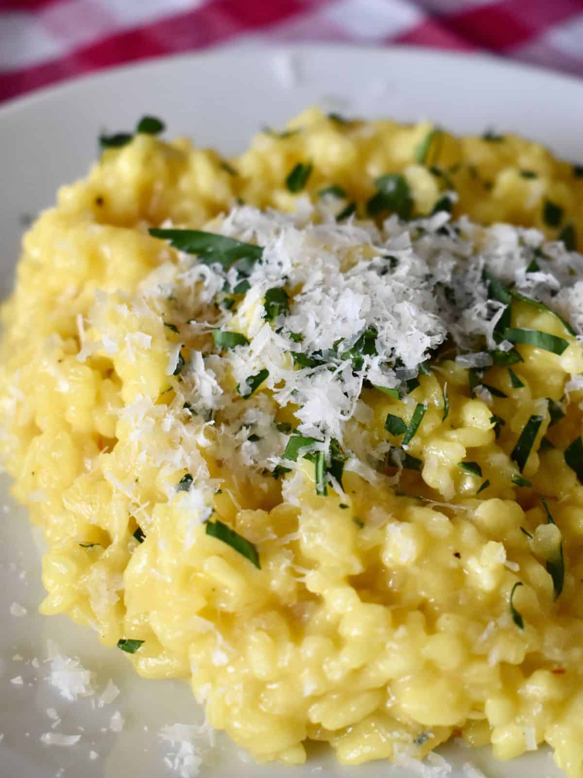 Risotto alla Milanese on a white plate with parmesan and parsley on top. 