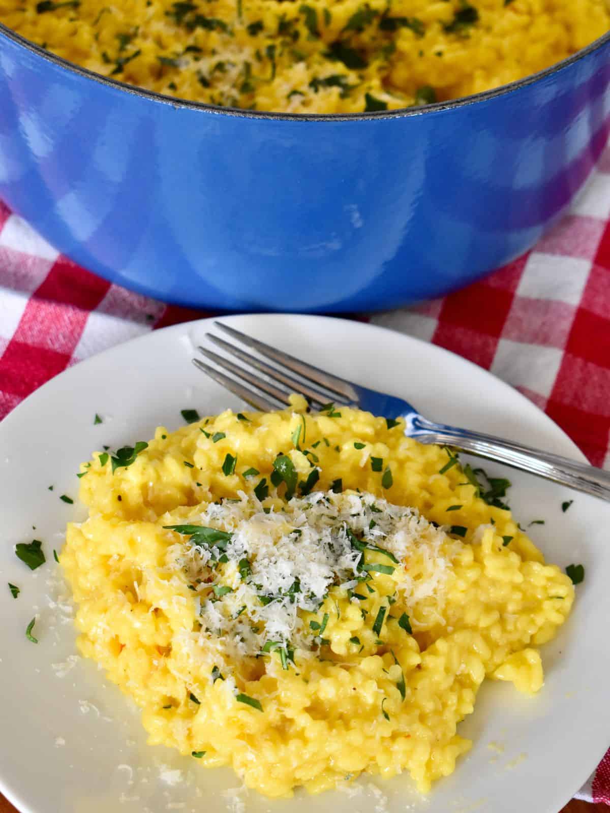 Risotto alla Milanese on a white plate and dutch oven in the background.
