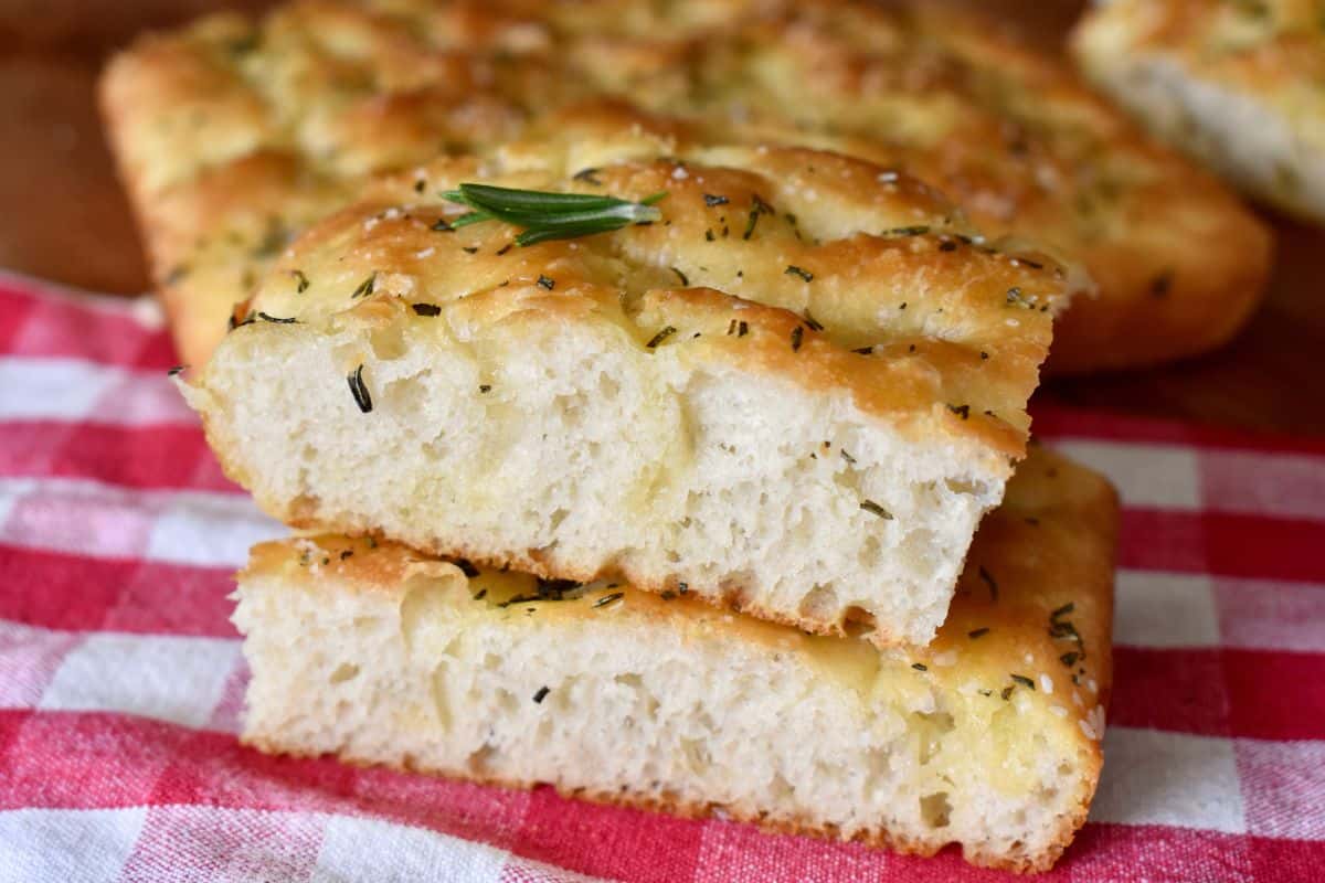 Two slices of focaccia bread stacked on each other with a sprig of rosemary on top. 