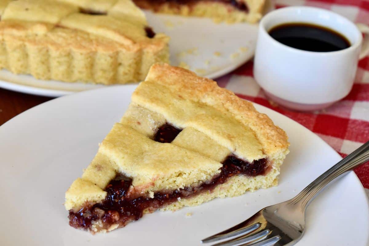 Italian Crostata slice with strawberry jam filling on a round white plate. 